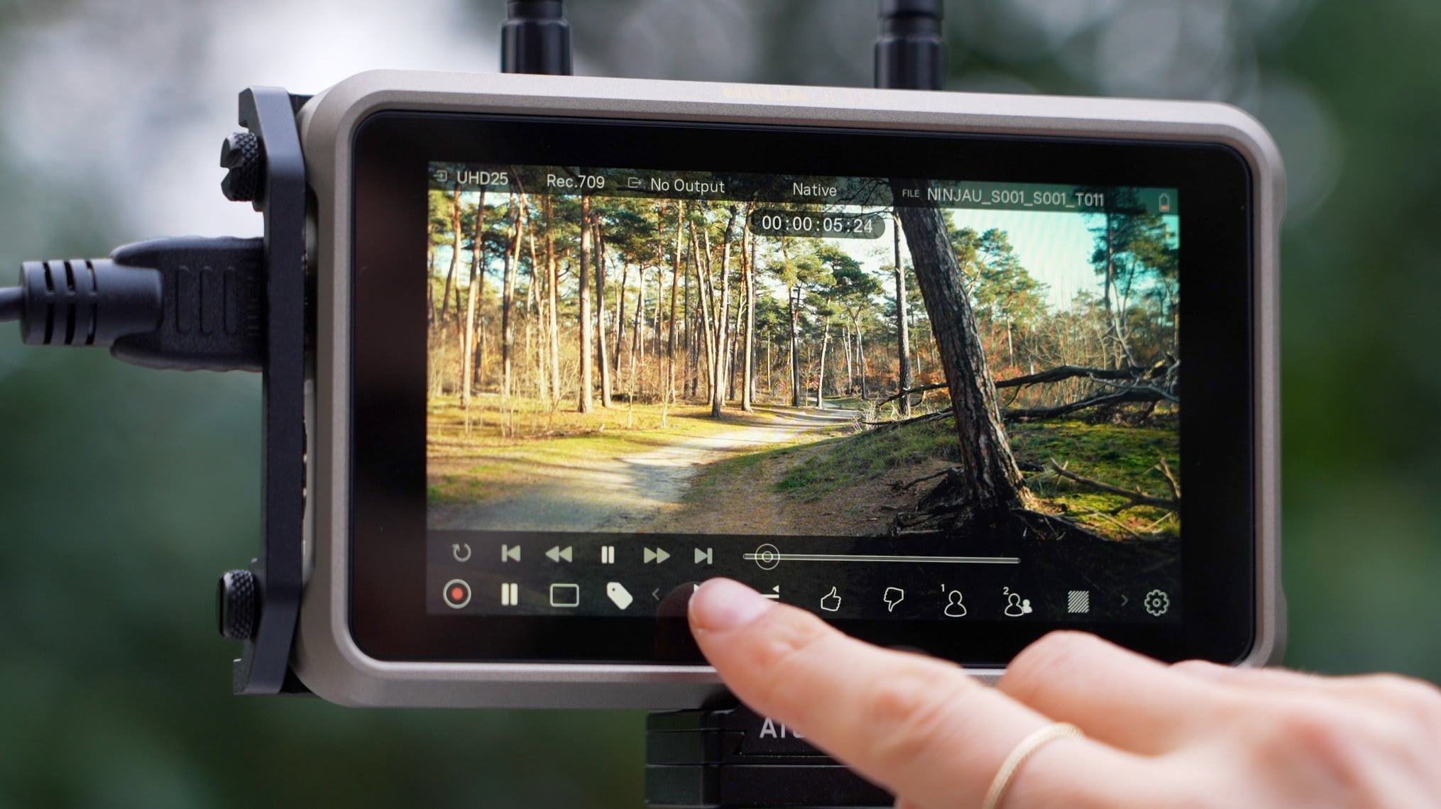 Ein Finger bedient den Touchscreen des Atomos Ninja Ultra mit einer angezeigten Waldaufnahme